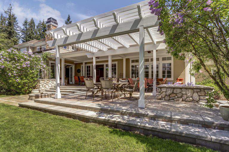 Lovely outdoor deck patio space with white dining pergola in the backyard of a luxury house.