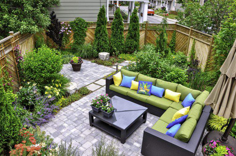 A beautiful small, urban backyard garden featuring a tumbled paver patio, flagstone stepping stones, and a variety of trees, shrubs and perennials add colour and year round interest.